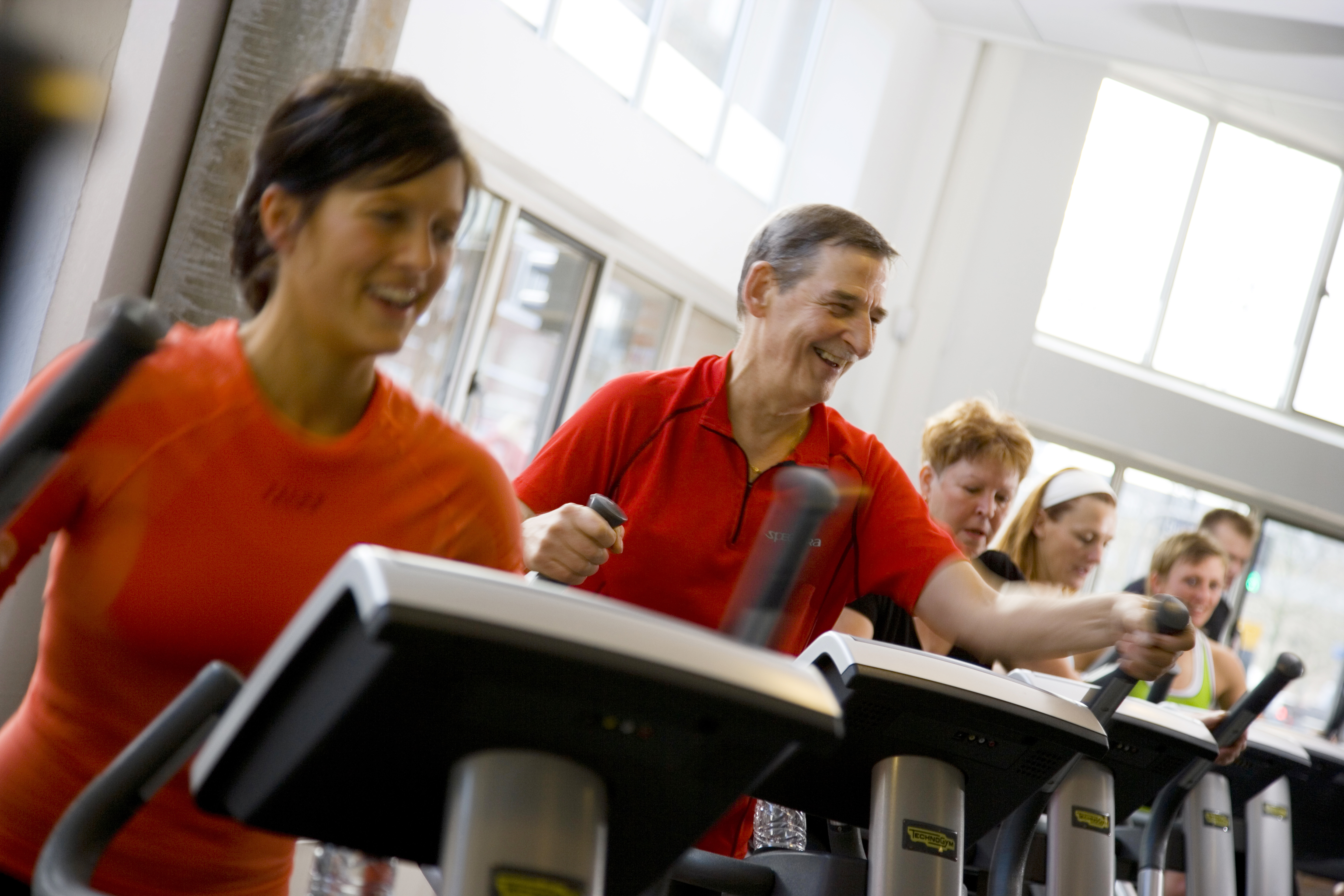 En flok mennesker i en traeningssal faar dyrket motion på crossmaskinen.