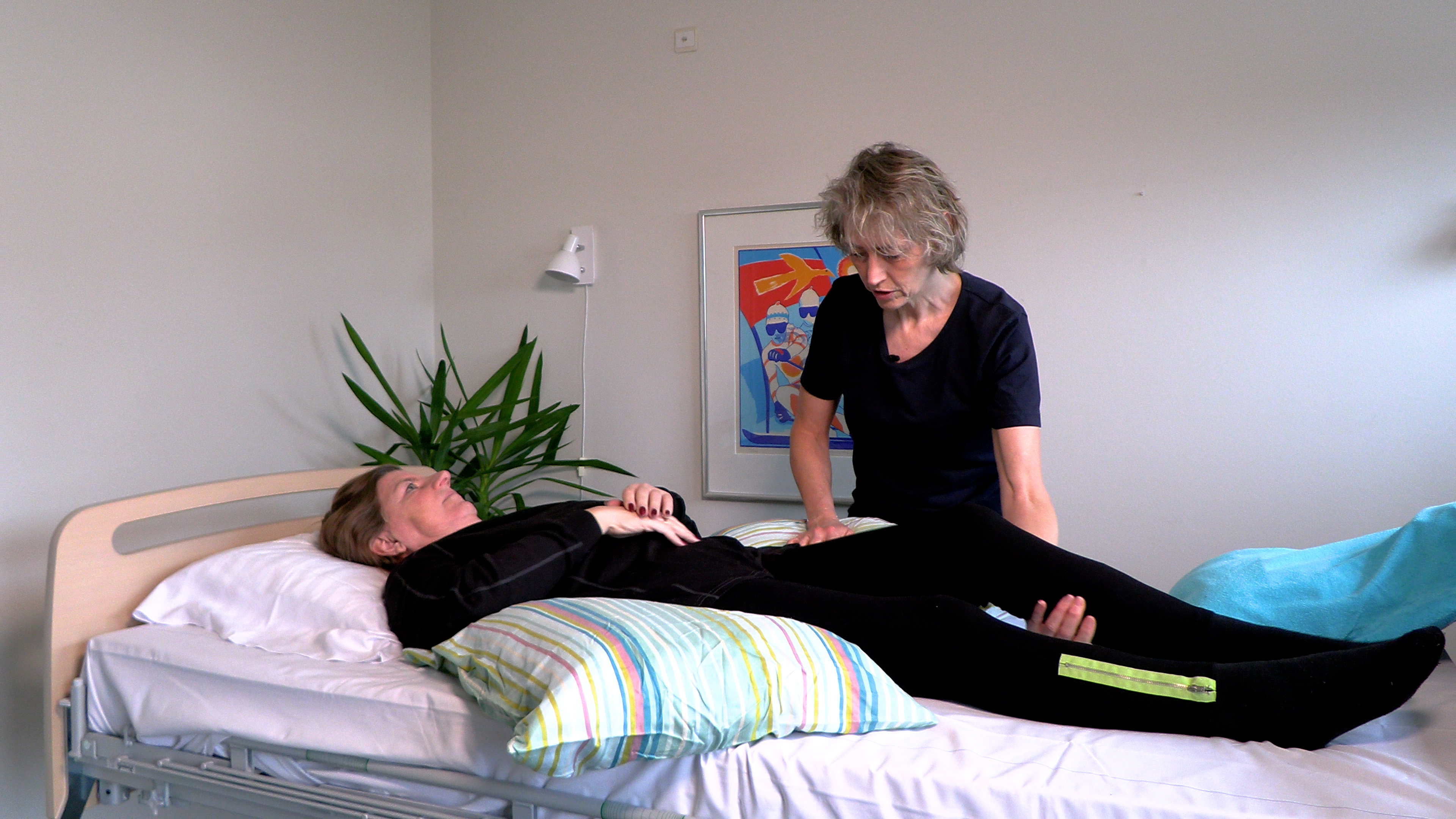 Billede fra lejringsvideo, hvor fysioterapeut viser, med hjælp fra en patient, hvordan man aflaster hael og bagdel