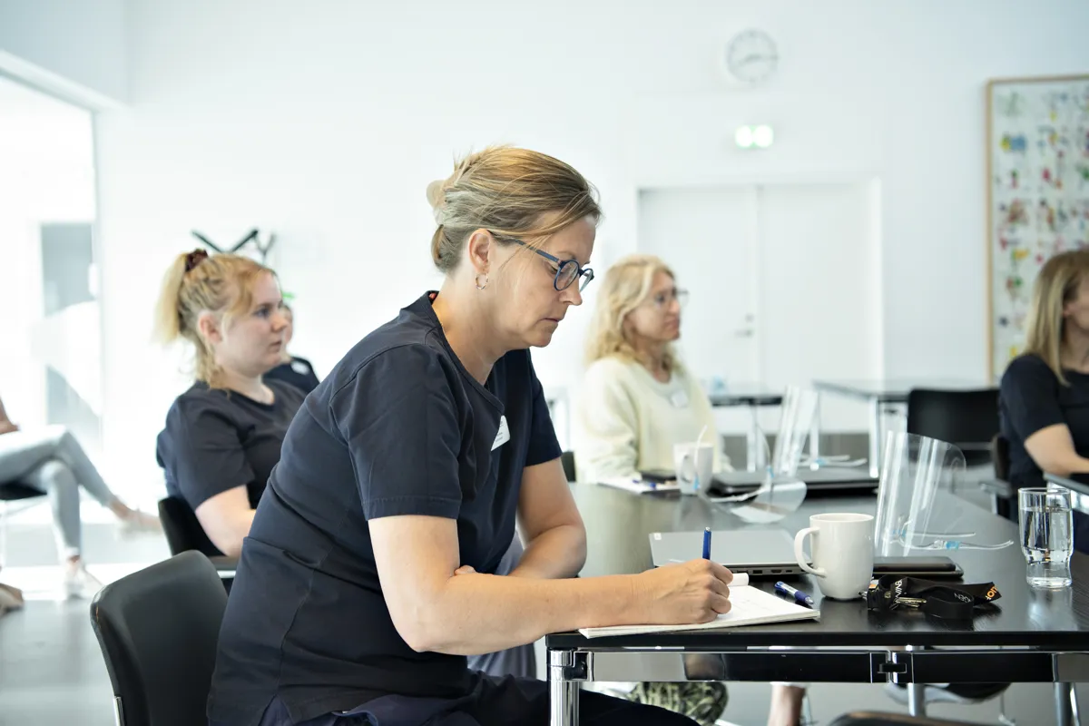 Personalemedlemmer sidder til møde og lytter og tager noter
